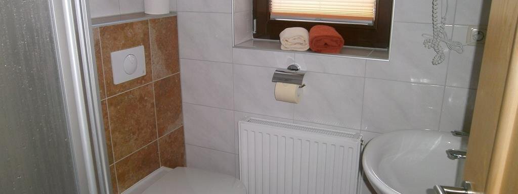 A small bathroom with a shower, toilet, and sink. It has bright tiles and a windowsill with towels. - Hirschenhof - Sölden