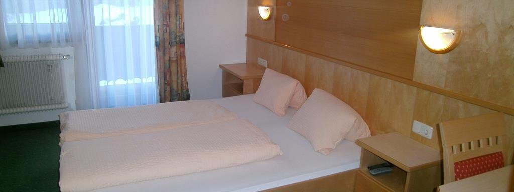 Hausbilder Hirschenhof 037 A simple hotel room with a double bed, a table, and a television. The wall is friendly designed and there is plenty of daylight through the window. - Hirschenhof - Sölden