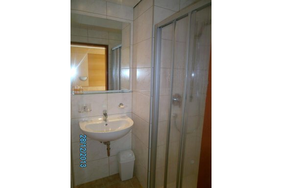 A small bathroom with a sink and a shower. The walls are tiled and there is a mirror above the sink. - Hirschenhof - Sölden