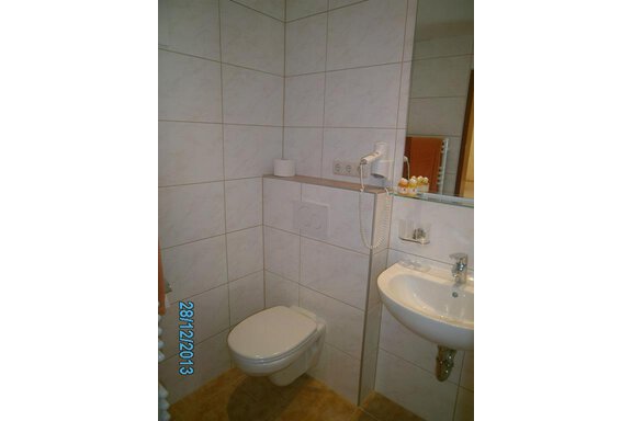 A simple bathroom with a toilet and a sink. White tiles on the walls and a mirror are also present. - Hirschenhof - Sölden