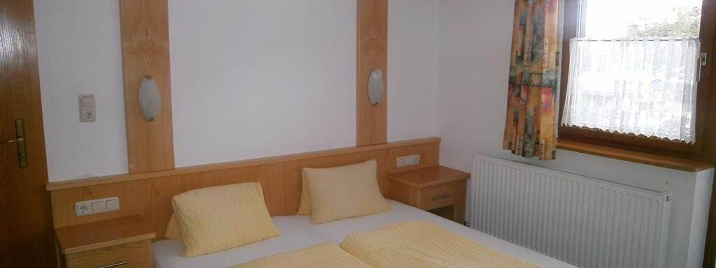 Hausbilder Hirschenhof 041 A simple bedroom with a double bed and yellow pillows. There is a bedside table and a window with curtains. - Hirschenhof - Sölden