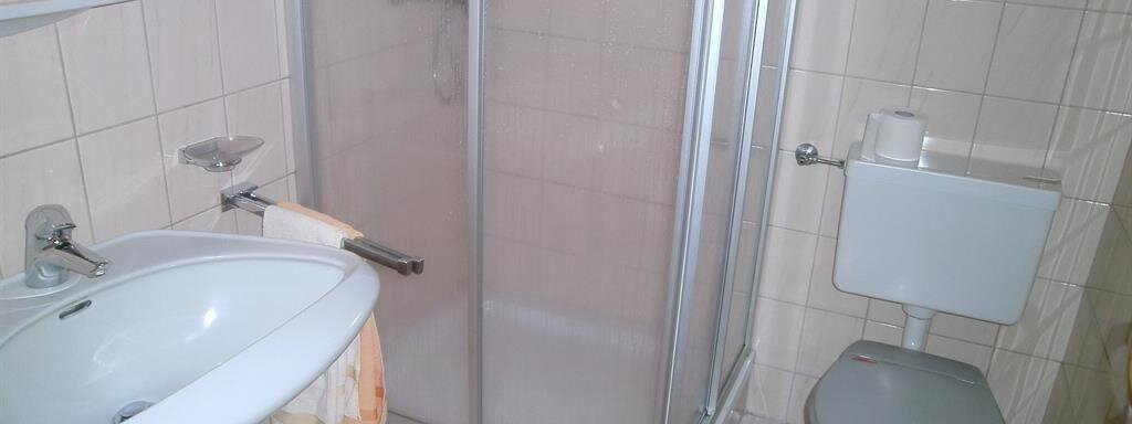 A simple bathroom with a shower, a sink, and a toilet. The walls are covered with light tiles. - Hirschenhof - Sölden