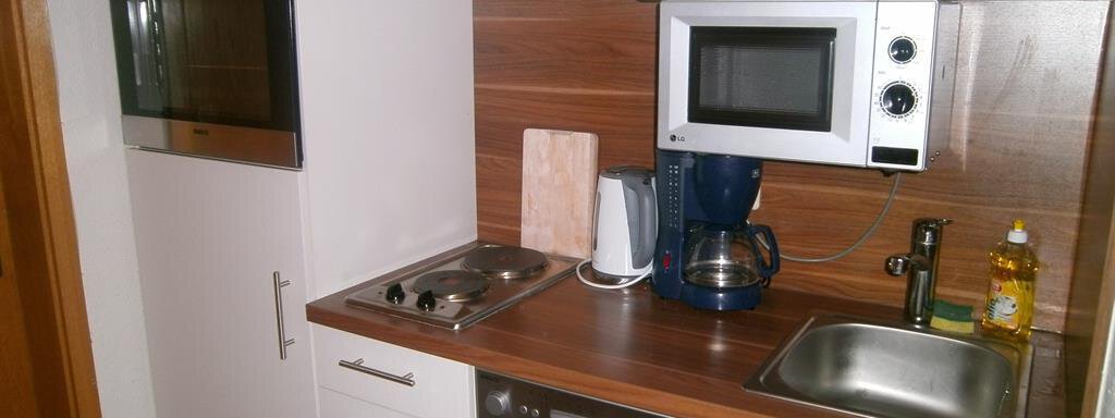 A modern kitchen with white cabinets and wooden elements. It is equipped with a stove, microwave, and coffee machine. - Hirschenhof - Sölden