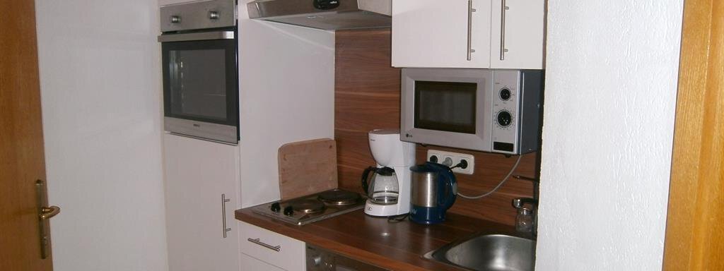 A small, modern kitchenette with white cabinets and wood details. Appliances like a stove, an oven, and a coffee maker are well arranged. - Hirschenhof - Sölden
