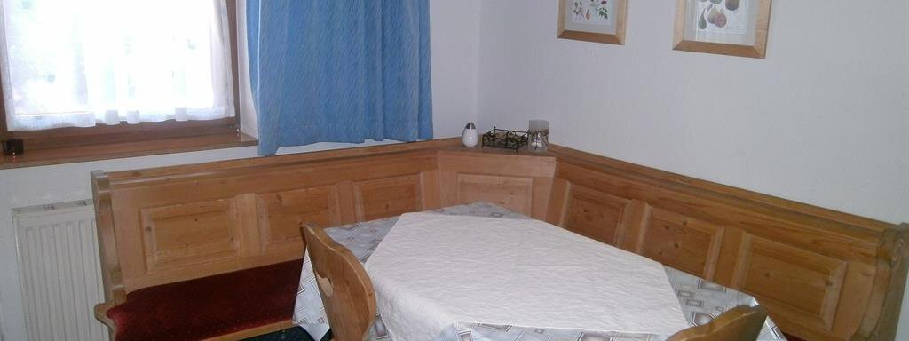 A cozy dining area with a round table and wooden bench. The window lets in plenty of light and the walls are decorated with pictures. - Hirschenhof - Sölden