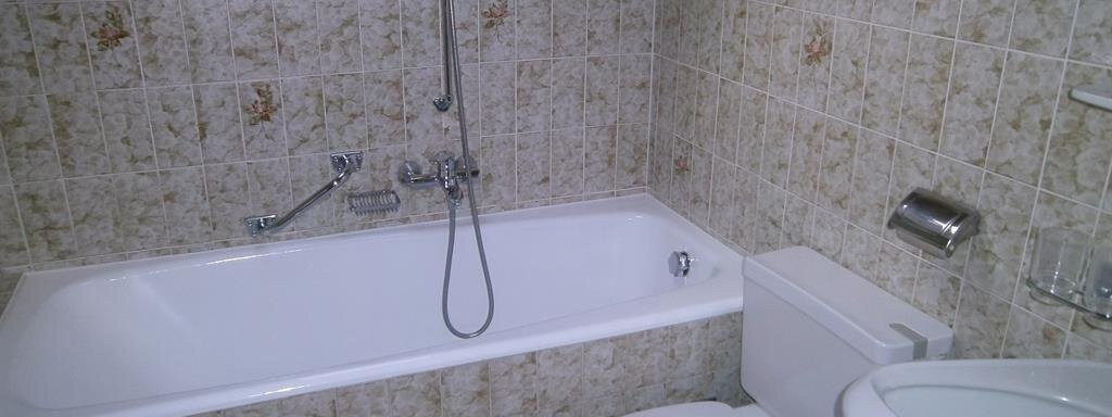 A simple bathroom with a bathtub, a toilet, and a sink. The walls are designed with tiled, light patterns. - Hirschenhof - Sölden
