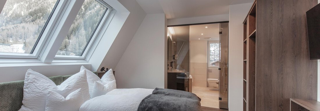 A modern furnished bedroom with large windows and a cozy bed. The room features a warm wooden floor and pleasant lighting. - Home4You - Sölden