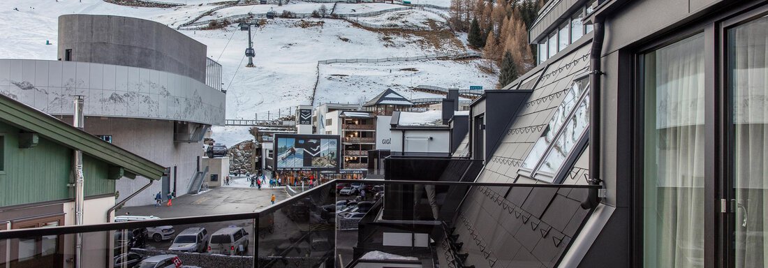 A modern balcony overlooking a snow-covered mountain landscape. In the background, ski lifts and buildings in a winter sports resort can be seen. - Home4You - Sölden