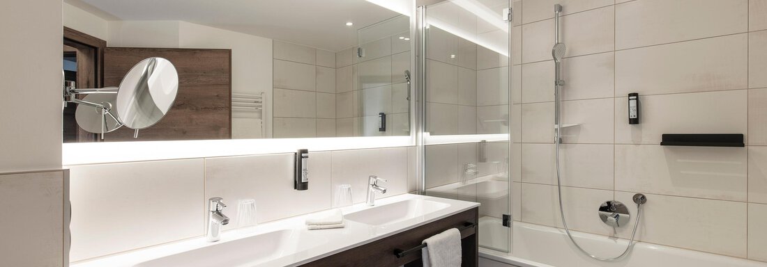 A modern bathroom with two sinks and a large mirror. The neutral colors and the illuminated wall create a stylish atmosphere. - Home4You - Sölden