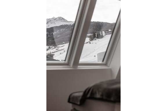 A view from a window of a snow-covered landscape with mountains in the background. In the foreground, a cozy seating area is visible. - Home4You - Sölden