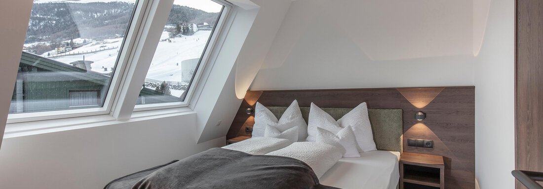 A modern bedroom with a large bed and cozy pillows. Through the windows, one can see snow-capped mountains. - Home4You - Sölden