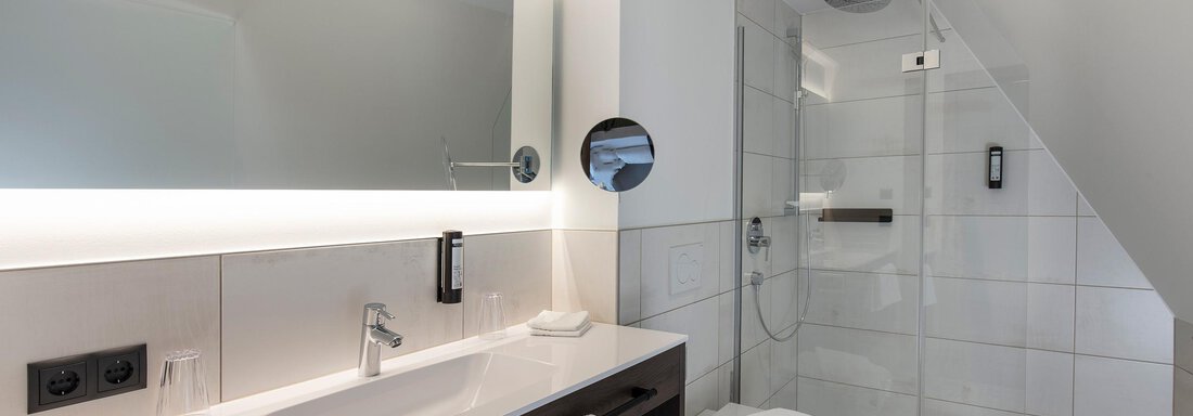A modern bathroom with a stylish sink and a large mirror. The shower is made of glass and the space is bright and inviting. - Home4You - Sölden