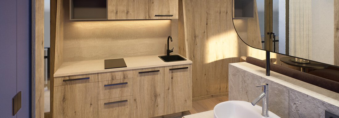 A modern bathroom with wooden-paneled cabinets and an elegant washbasin. The warm light creates a cozy atmosphere. - Hotel Alpina - Sölden