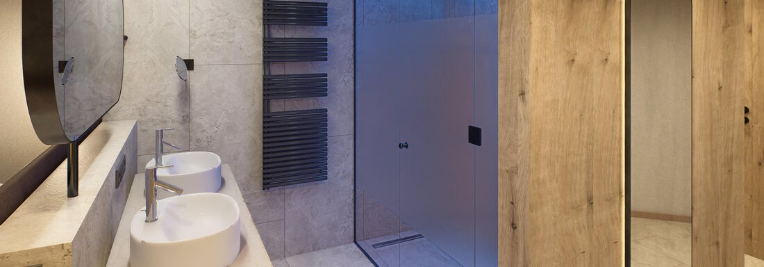 A modern bathroom with two sinks and a spacious shower. The walls are brightly tiled, and natural materials create a pleasant atmosphere. - Hotel Alpina - Sölden
