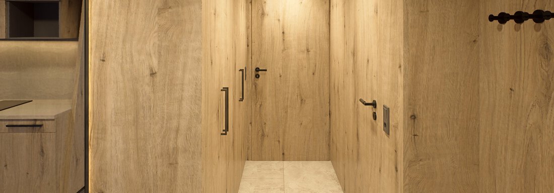 A modern hallway with wooden paneling and light walls. The floor is brightly tiled, and there are wall lights along the corridor. - Hotel Alpina - Sölden