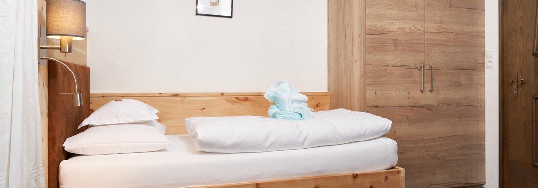A simple bedroom with a single bed and wooden furniture. There is a wardrobe and a lamp for soft lighting. - Hotel am Hof - Sölden