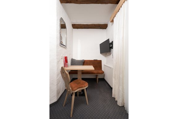 A small, cozy dining room with a wooden bench and a table. On the wall, there is a television and a mirror. - Hotel am Hof - Sölden
