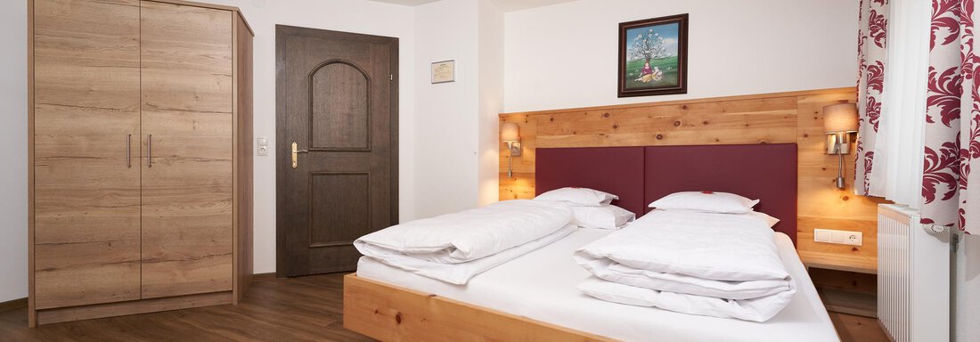 A cozy bedroom with a double bed and wooden furniture. The walls are bright, and a colorful picture decorates the room. - Hotel am Hof - Sölden