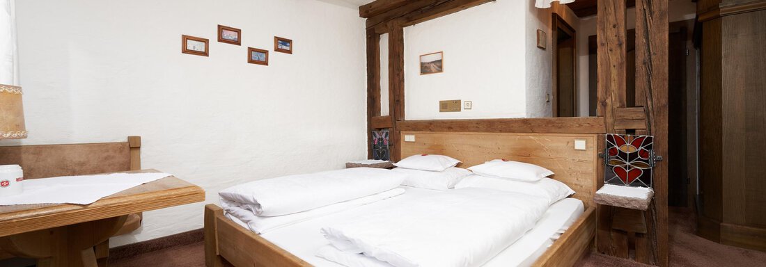 A cozy bedroom with wooden details and two single beds. There is also a small table and chairs in a rustic atmosphere. - Hotel am Hof - Sölden