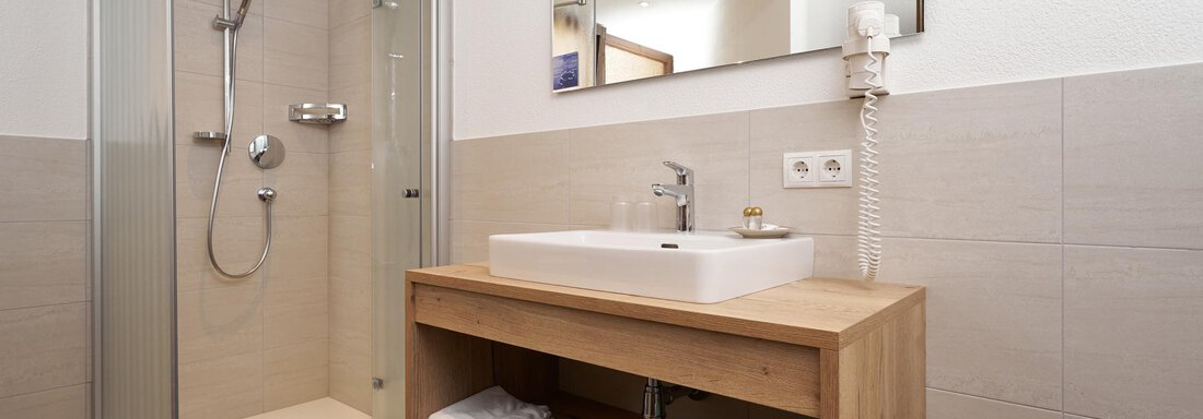 A modern bathroom with a glass shower and a minimalist wooden sink. Towels are neatly stored, and the space feels bright and inviting. - Hotel am Hof - Sölden
