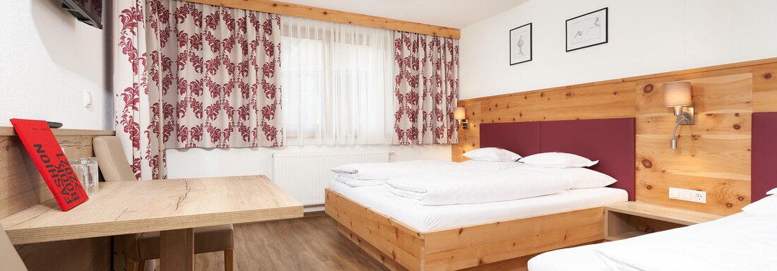 A cozy hotel room with wooden furniture and two single beds. Large windows provide plenty of daylight and a pleasant atmosphere. - Hotel am Hof - Sölden