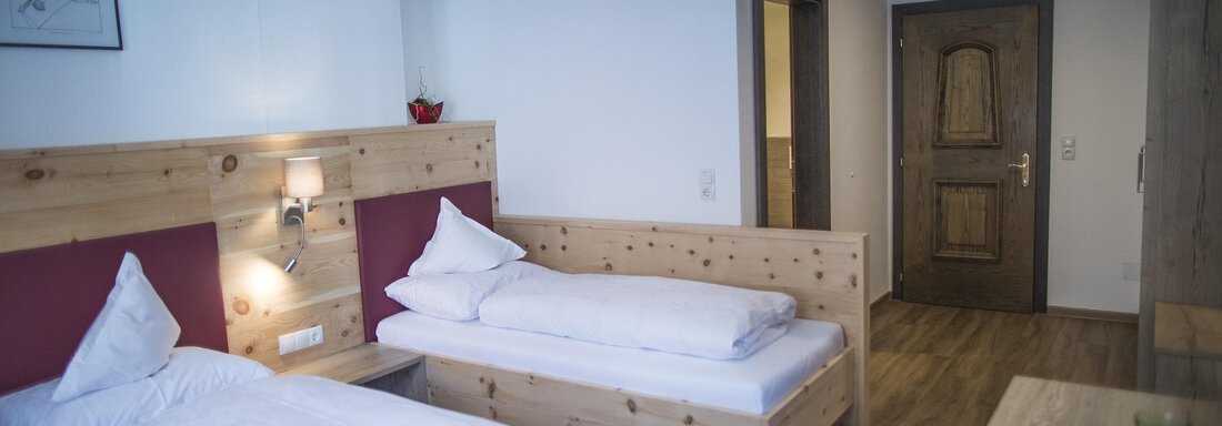A modern bedroom with two wooden single beds. The room is bright and cheerful, with a table and a door leading to a hallway. - Hotel am Hof - Sölden