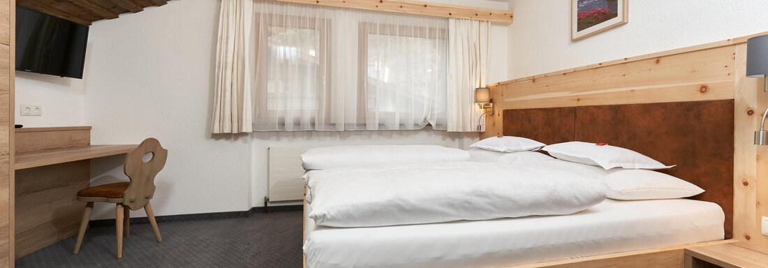 A modern bedroom with two beds and wooden furniture. Large windows provide plenty of daylight. - Hotel am Hof - Sölden