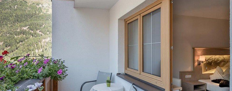 A cozy balcony with two chairs and a small table. In the background, blooming plants and mountains can be seen. - Hotel Elisabeth - Sölden