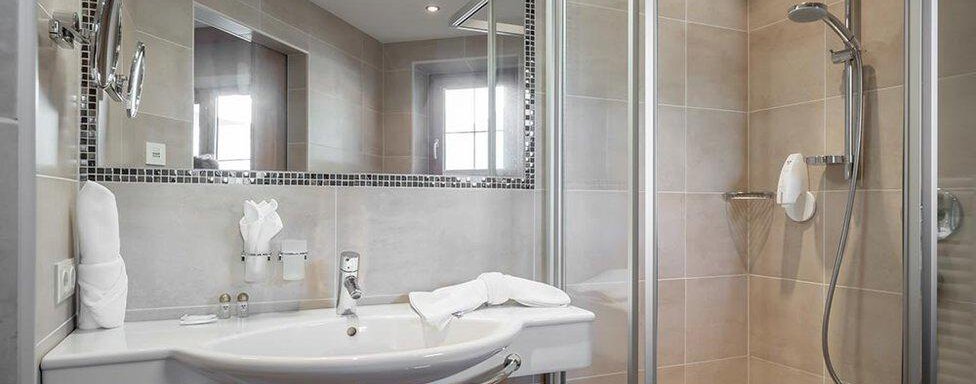 A modern bathroom with a shower and large mirrors. The bright tiles and towels create a clean impression. - Hotel Elisabeth - Sölden