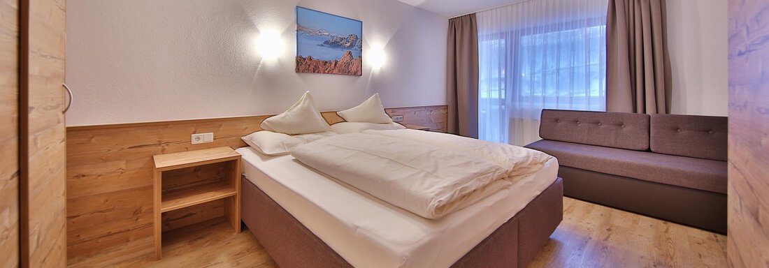 Zimmer5 A modern bedroom with a large bed and a cozy seating area. The walls are light, and there is a window with curtains. - Haus Söldenblick - Sölden