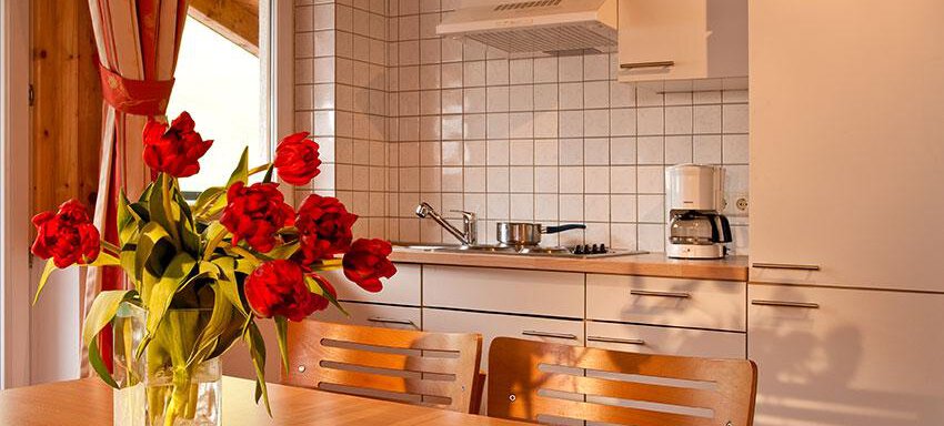 Wohnküche A modern kitchen with white furniture and a wooden ceiling. On the table, there is a vase with red tulips. - Hotel Garni Ehrenreich - Sölden