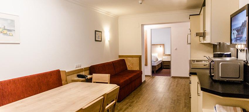 A modern room with a seating area and a table. The well-equipped kitchen is also visible, and in the background, a door leads to another room. - Hotel Garni Ehrenreich - Sölden
