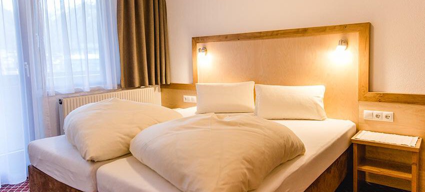 A cozy bedroom with two single beds and white bedspreads. Large windows let in plenty of daylight. - Hotel Garni Ehrenreich - Sölden