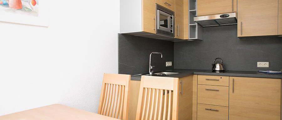 Wohnküche A modern kitchen with wooden cabinets and clean lines. A table with chairs is visible in the foreground. - Hotel Garni Ehrenreich - Sölden