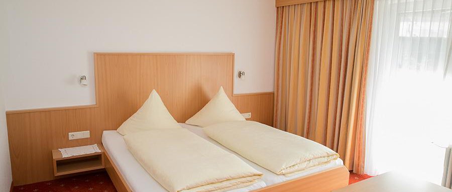 A simple hotel room with a double bed and bright, cozy colors. Large windows provide plenty of daylight. - Hotel Garni Ehrenreich - Sölden