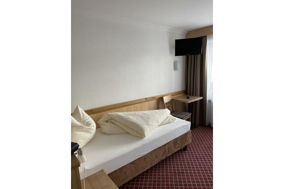 A simple hotel room with a double bed and two pillows. There is a television and a table next to a window. - Hotel Garni Ehrenreich - Sölden