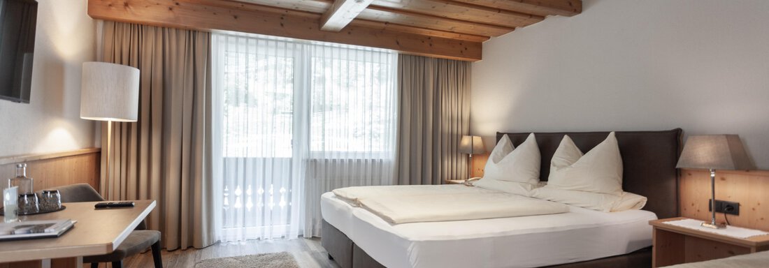 A modern hotel room with two beds and wooden ceilings. Large windows let in a lot of light and create an inviting atmosphere. - Hotel Hubertus - Sölden