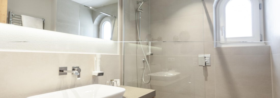 A modern bathroom with a large shower cubicle and an elegant washbasin. Bright tiles and a window create a friendly atmosphere. - Hotel Hubertus - Sölden