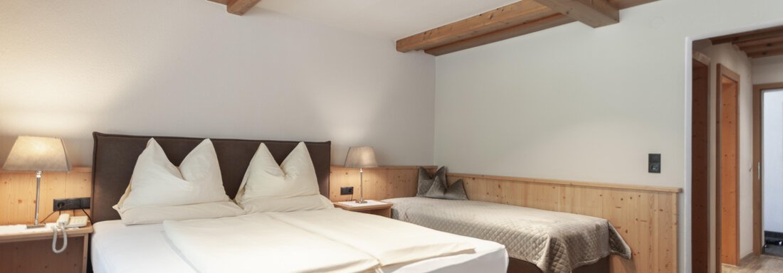 A modern room with two beds and an additional sofa bed. The warm wooden details give the space a cozy atmosphere. - Hotel Hubertus - Sölden