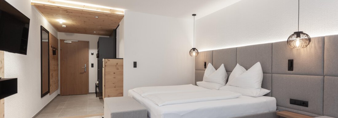 A modern hotel room with a large bed and elegant decor. The warm wood and gray tones create a cozy atmosphere. - Hotel Hubertus - Sölden