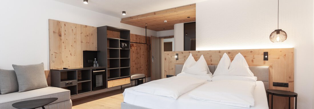 A modern bedroom with two beds and wooden elements. There is a cozy seating area and a small kitchenette. - Hotel Hubertus - Sölden