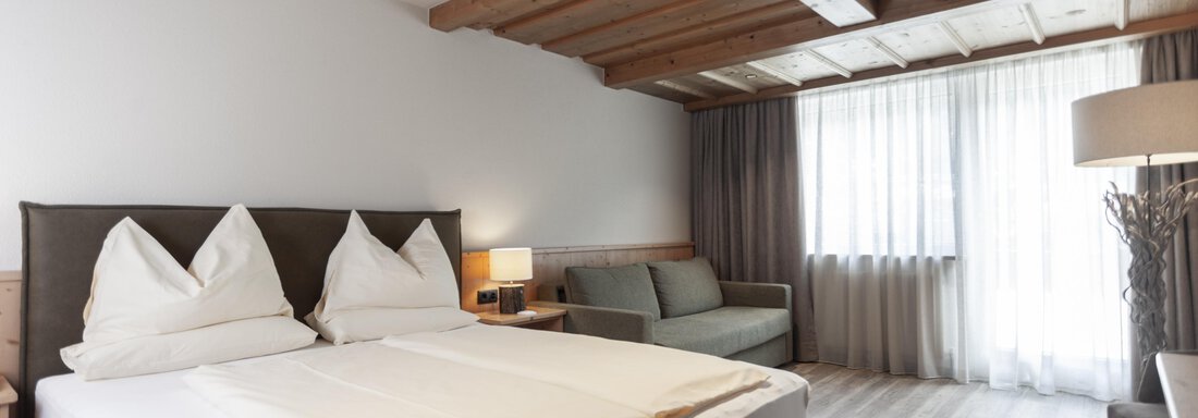 A modern hotel room with a large double bed and two comfy pillows. The room has large windows that let in plenty of natural light. - Hotel Hubertus - Sölden