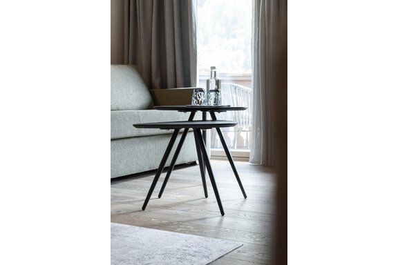 An elegant table with three legs stands in a modern room. Next to the table are a glass of water and a glass bottle. - Hotel Hubertus - Sölden