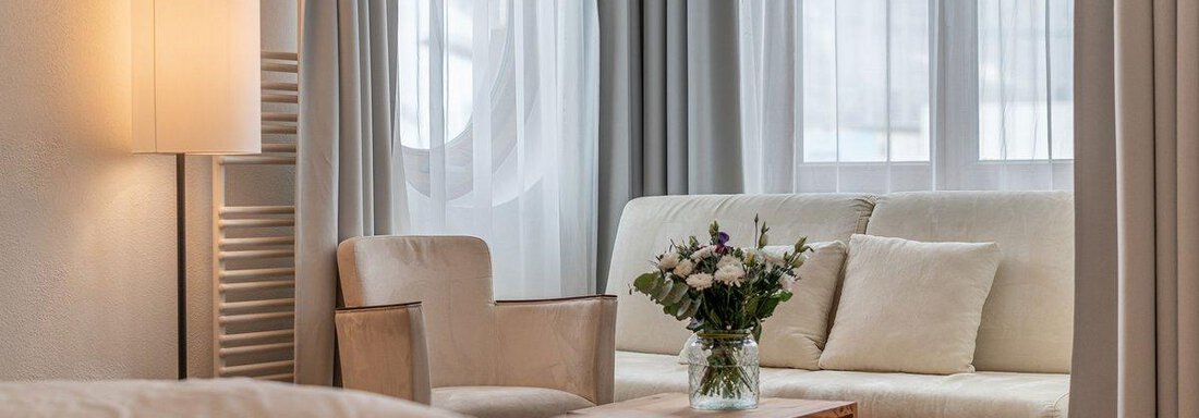 A welcoming living room with a comfortable sofa and an armchair. On the table is a vase with fresh flowers, and the windows let in plenty of natural light. - Hotel Liebe Sonne - Sölden