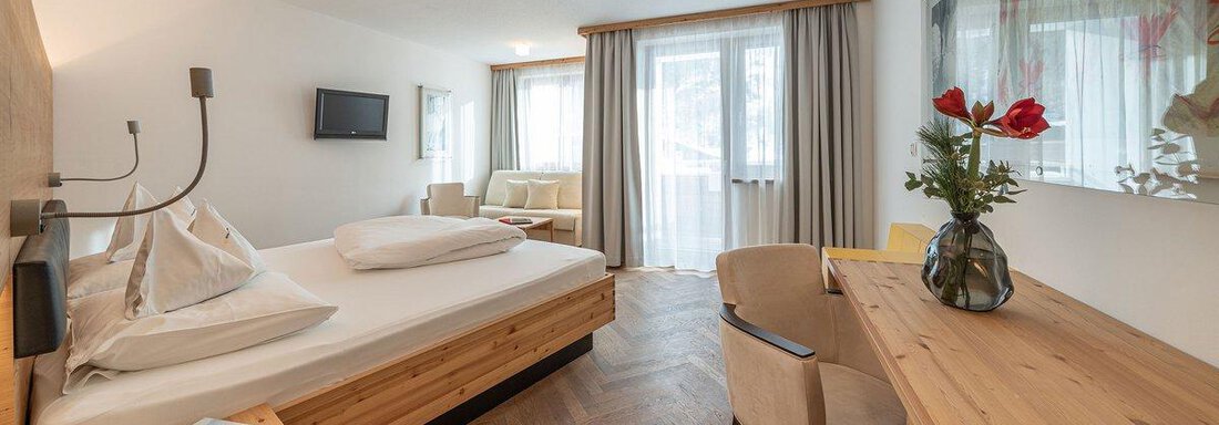 A modern room with a double bed, a desk, and a cozy seating area. Large windows let in plenty of light and provide a view outside. - Hotel Liebe Sonne - Sölden