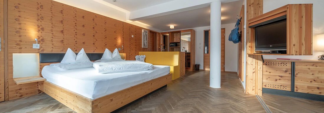 Hotel Liebe Sonne Suite Wildspitze | © Hotel Liebe Sonne (CC C) A modern room with wooden paneling and a large bed. It includes a cozy seating area and a television. - Hotel Liebe Sonne - Sölden
