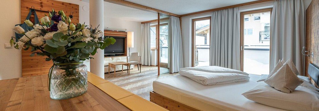 A modern bedroom with large windows and light wood interior. On the table is a vase with flowers that gives the room a cozy atmosphere. - Hotel Liebe Sonne - Sölden