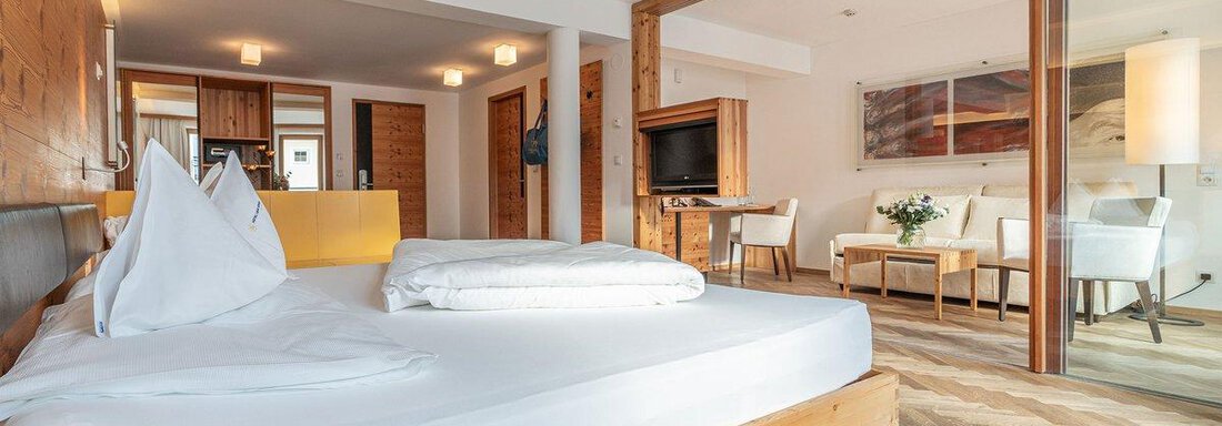 A modern hotel room with a large bed and a cozy seating area. The decor is bright and inviting, with wooden accents and natural colors. - Hotel Liebe Sonne - Sölden