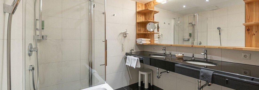 A modern bathroom with a shower and a bathtub. The vanity is made of wood and has large mirrors. - Hotel Liebe Sonne - Sölden