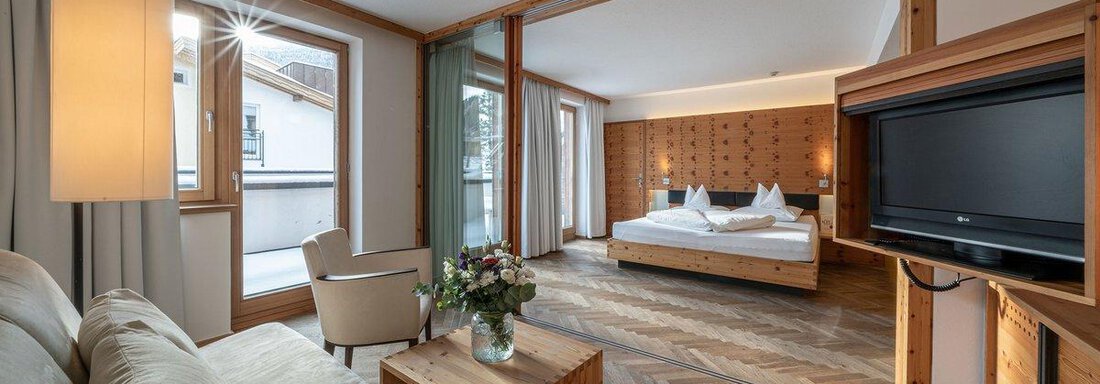 A modern room with wooden details and a cozy sofa. The bedroom is bright and inviting, with a large window and a floral arrangement on the table. - Hotel Liebe Sonne - Sölden